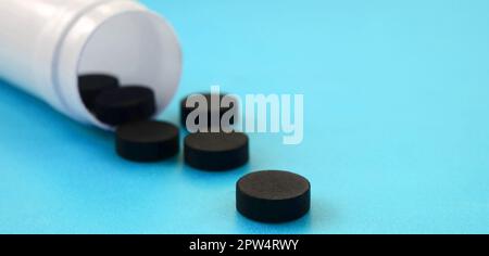 Diverse compresse nero ricade al di fuori del vaso in plastica sulla superficie blu. Immagine di sfondo sul farmaceutico e medico argomenti. Carbone attivo Foto Stock