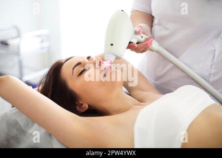 Dall'alto della cliente femminile sdraiata sul divano in bellezza salone durante l'epilazione laser del viso Foto Stock