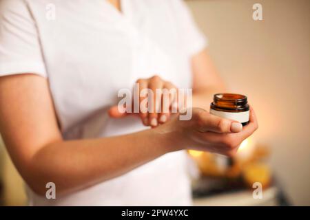 Irriconoscibile crop beautician femminile che applica la crema dal vaso sulla mano prima della procedura in salone Foto Stock