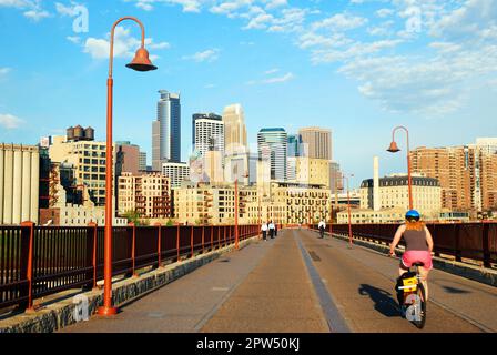 Un biciclista guida la sua bicicletta sopra lo Stone Arch Bridge, chiuso al traffico, e pedala verso lo skyline di Minneapolis Foto Stock