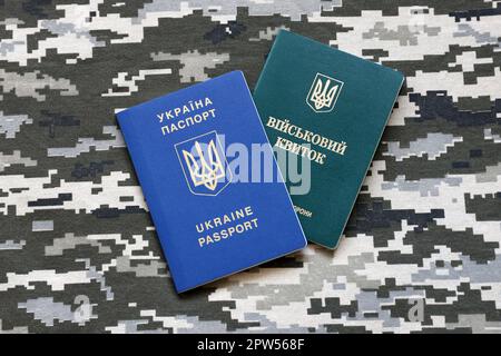 Documento d'identità militare ucraino e passaporto straniero su tessuto con tessuto di camouflage pixellato. Panno con motivo camo in pixel grigio, marrone e verde Foto Stock