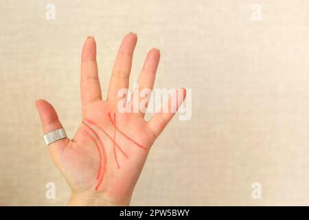 Primo piano del palmo femminile con linee di vita disegnate con penna rossa in feltro isolato su sfondo beige chiaro, spazio di copia per il testo. Palmistry, chiromancy Foto Stock