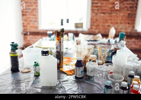 Interni moderni del laboratorio d'arte o studio. Secchi con vernice, vasetti di vetro sporchi, spazzole, pistola a spruzzo, solventi e altre forniture d'arte sono sul Foto Stock