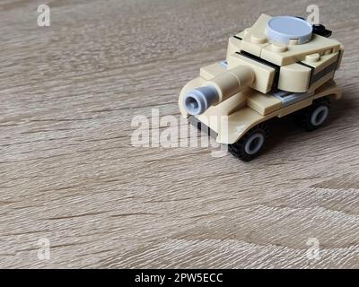 Serbatoio giocattolo su un tavolo di legno. Giocattolo di plastica. Artigianato da un designer per bambini. Il colore beige del serbatoio, un'immagine sfocata intorno ai bordi. Lezione che Foto Stock