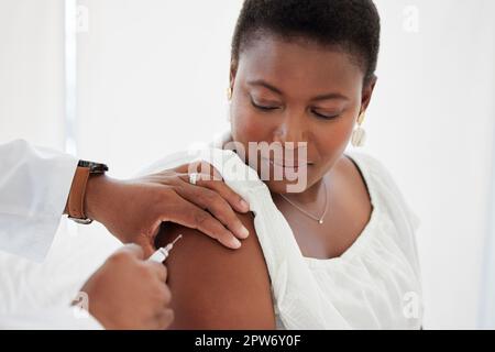 Donna afroamericana che ottiene iniettata nella clinica. Paziente focalizzato che guarda un medico tenere un ago con il vaccino. Paziente iniettato in Foto Stock