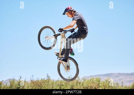 Giovane uomo che mostra le sue abilità ciclistiche mentre fuori in bicicletta su una bicicletta fuori. Adrenalina junkie praticare un salto di sporcizia all'aperto. Maschio che indossa un casco Foto Stock