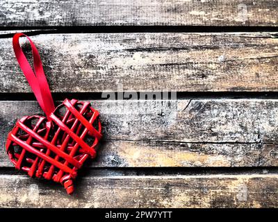 Cuore di vimini rosso d'amore su sfondo a trama di legno. Biglietto di auguri per San Valentino. Vista dall'alto con spazio di copia. Cuore di vimini rosso fatto di ramoscelli o paglia. F Foto Stock