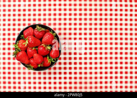 Vista del piano portapaziente, nero piccolo vaso in ceramica di fragole sul rosso Gingham a scacchi la tovaglia Foto Stock