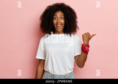 Un colpo di testa di donna scura con pelle sorridente felicemente e che batte da parte mentre si alza sopra il rosa. Foto Stock