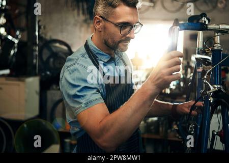 Un altro giorno, un altro restauro di biciclette. un uomo maturo che lavora in un negozio di riparazione di biciclette. Foto Stock