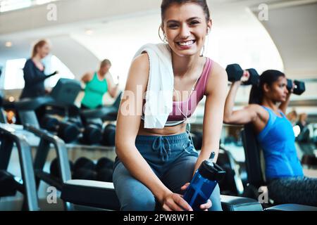 La musica mi motiva. Ritratto corto di una giovane donna attraente che prende una pausa dal suo allenamento in palestra. Foto Stock