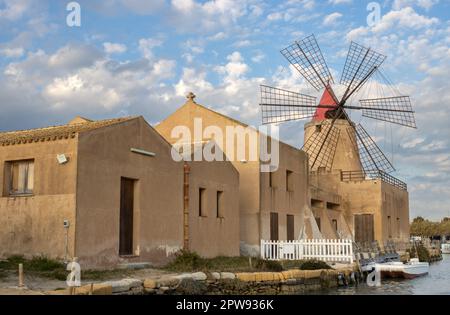 Saline e mulini a vento per la lavorazione del sale marino. Canale tra loro. Cielo blu con nuvole bianche in primavera. Laguna dello Stagnone, Marsala, SIC Foto Stock