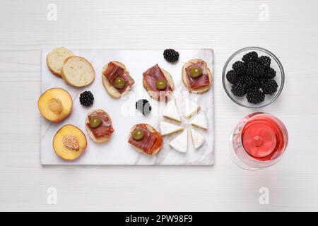 Bicchiere di delizioso vino rosato e spuntini su un tavolo di legno bianco, piatto Foto Stock