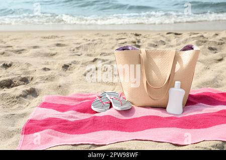 Asciugamano a strisce rosa con borsa, infradito e crema solare sulla spiaggia Foto Stock