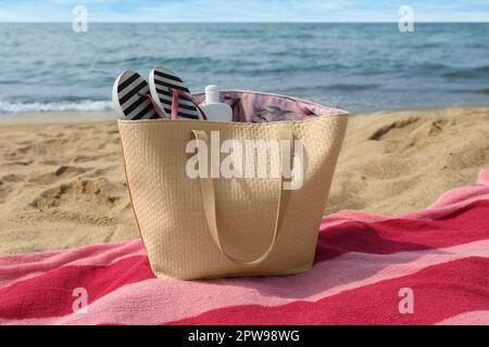 Asciugamano a strisce rosa con borsa, infradito e crema solare sulla spiaggia Foto Stock