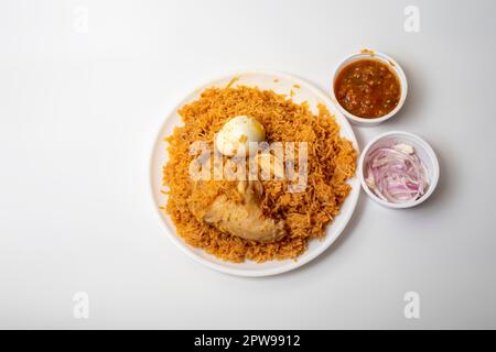 Cibo indiano piccante pollo biryani caldo con uova, raita e cipolla su piatto su sfondo bianco. Foto Stock