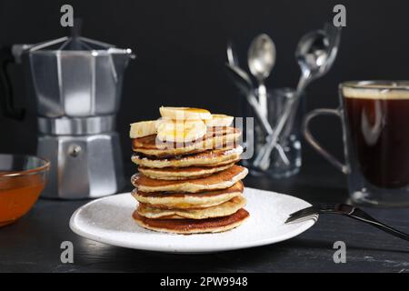 Piatto di frittelle alla banana con miele e zucchero a velo servito sul tavolo nero Foto Stock