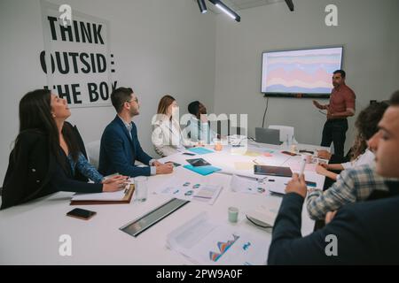 Uomo d'affari più anziano che ha una presentazione e che parla con i suoi colleghi mentre si trova accanto alla tv nello spazio di lavoro del co Foto Stock
