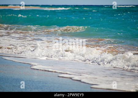 Le onde colpiscono dolcemente la spiaggia di sabbia creando un bellissimo getto dalle acque blu precedentemente turchesi Foto Stock
