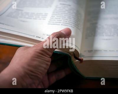 Un pollice che capovolgerà le pagine di un libro in fuoco poco profondo, priorità bassa educativa Foto Stock