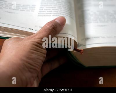 Un pollice che capovolgerà le pagine di un libro in fuoco poco profondo, priorità bassa educativa Foto Stock