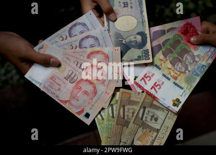 Bambino asiatico in possesso di rupia indonesiana, dollaro di Singapore, arabia Saudita riyal, e Giappone Yen denaro, poco focus Foto Stock