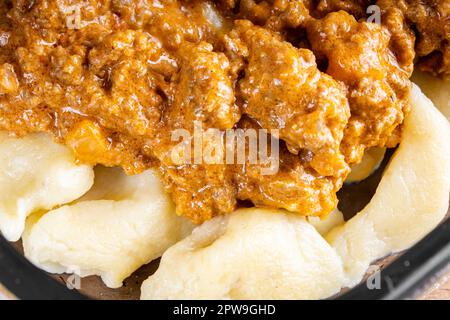 GNOCCHI COTTI CON CARNE MACINATA IN SALSA DI POMODORO, RICOPERTI DI FORMAGGIO GRATTUGIATO MONTATO SU UN PIATTO DI VETRO. Foto Stock