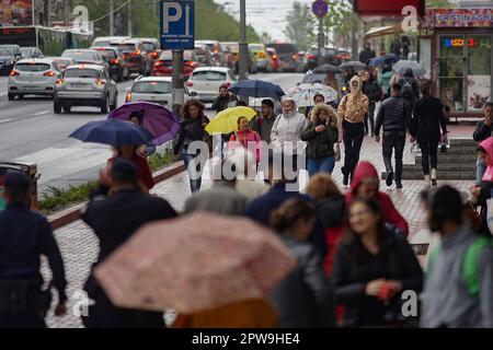 Bucarest, Romania. 27th aprile, 2023: Le persone con ombrelloni camminano per strada nonostante il tempo piovoso in una zona affollata del centro di Bucarest. Foto Stock