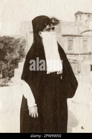 Egitto. Circa 1918. Una giovane donna che si posa per una fotografia, indossando al-habara, composta da una gonna a tutta lunghezza, una copertura per la testa, e una al-burqu’ bianca, una copertura per il viso. Foto Stock