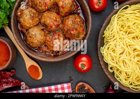 vista dall'alto gustosa zuppa di polpette in ciotola spaghetti in ciotola pomodori cucchiaio di legno sul tavolo Foto Stock
