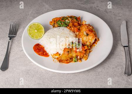 Deliziosa moqueca di pesce brasiliana con pomodoro, cipolla, olio d'oliva, coriandolo e semi di orocum. Servito su un piatto di porcellana bianca con riso. Foto Stock