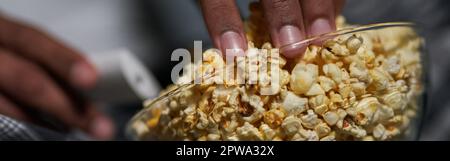 Buon gusto. Primo piano di mano maschile prendendo alcuni popcorn da una ciotola Foto Stock