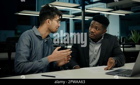 Diversi uomini d'affari afro-americani indiani uomini parlando di progetto on-line sul computer sedersi alla scrivania ufficio due multirazziale 30s colleghi maschi Foto Stock