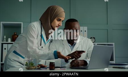 I colleghi medici multirazziali discutono di lavoro di squadra l'uomo africano e la donna araba due medici professionisti parlano di controllo sanitario MRI scansione Foto Stock