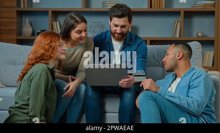 Squadra eccitata uomini diversi donne utilizzare la carta di credito per il pagamento online sul laptop multietnico gruppo di uomini d'affari amici colleghi vincitori celebrare Foto Stock