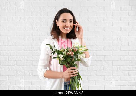 Giovane donna con fiori di alstroemeria su sfondo di mattoni bianchi Foto Stock