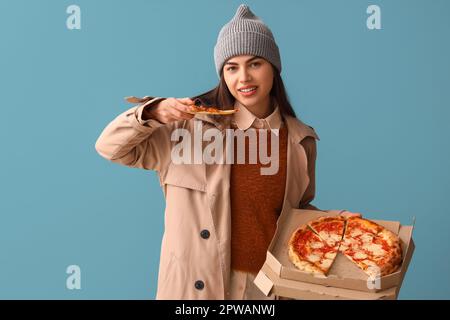 Giovane donna in cappello con scatola di gustosa pizza su sfondo blu Foto Stock