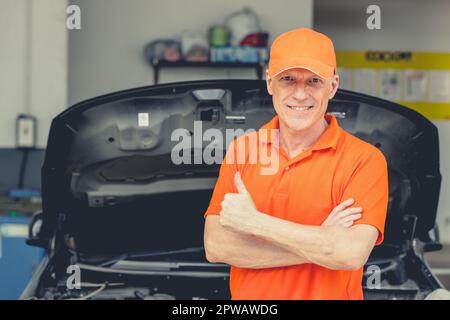 Meccanico di automobile di sguardo professionale anziano in piedi in garage. Ritratto felice sorridente caucasico adulto maschio in Auto Service Thumbs up. Foto Stock