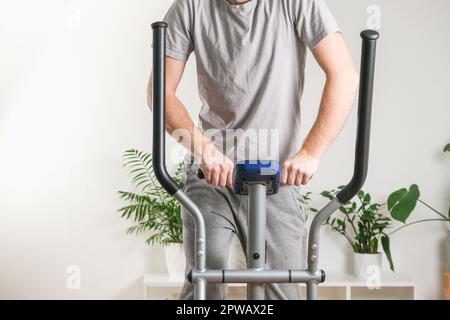Un uomo si allena su una macchina ellittica. Allenatore sportivo a casa in appartamento. Sport a casa. Foto Stock