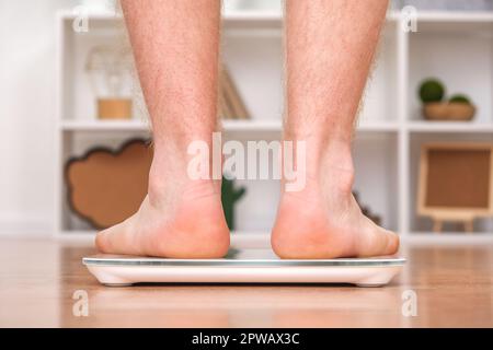 Un uomo si trova sulla bilancia. Il ragazzo sta pesando se stesso. Bilance da pavimento per la salute. Controllo del peso. Foto Stock