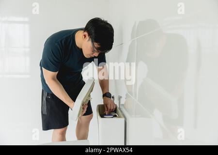 l'uomo che fa il lavoro domestico di chore è handyman che ripara il serbatoio della toletta nella stanza da bagno Foto Stock