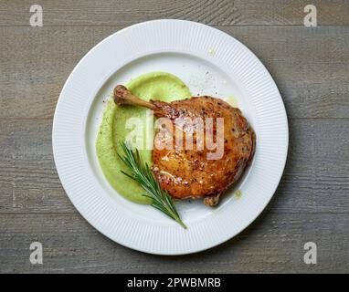 confit di coscia d'anatra e purea di broccoli su piatto bianco su tavolo di legno, vista dall'alto Foto Stock
