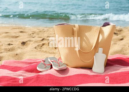 Asciugamano a strisce rosa con borsa, infradito e crema solare sulla spiaggia Foto Stock