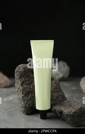 Tubo di crema per le mani tra le pietre su un tavolo grigio su sfondo scuro. Modello per il design Foto Stock