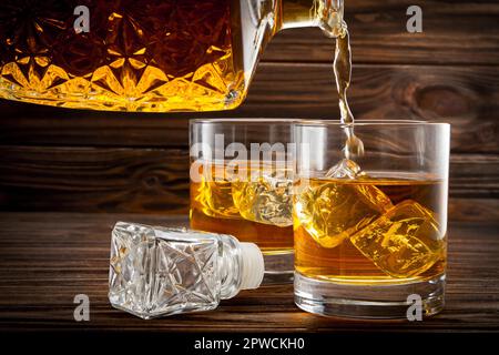 Versare il whiskey dalla bottiglia nei bicchieri su sfondo di legno Foto Stock