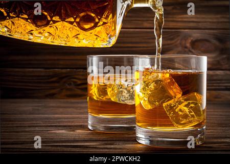 Versare il whiskey dalla bottiglia nei bicchieri su sfondo di legno Foto Stock