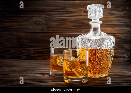 Bottiglia e due bicchieri con ghiaccio e whiskey su sfondo di legno Foto Stock