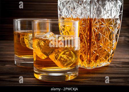 Primo piano di bottiglia e due bicchieri con ghiaccio e whiskey su fondo in legno Foto Stock