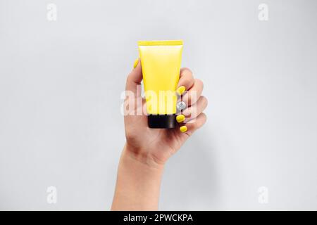 Vista dall'alto di una donna anonima con una mano curata che mostra il vuoto tubo di crema su sfondo grigio chiaro Foto Stock