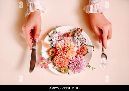 Vista dall'alto di una femmina anonima con taglio a forchetta e a coltello e mangiare fiori naturali su piatto contro sfondo di pesca Foto Stock